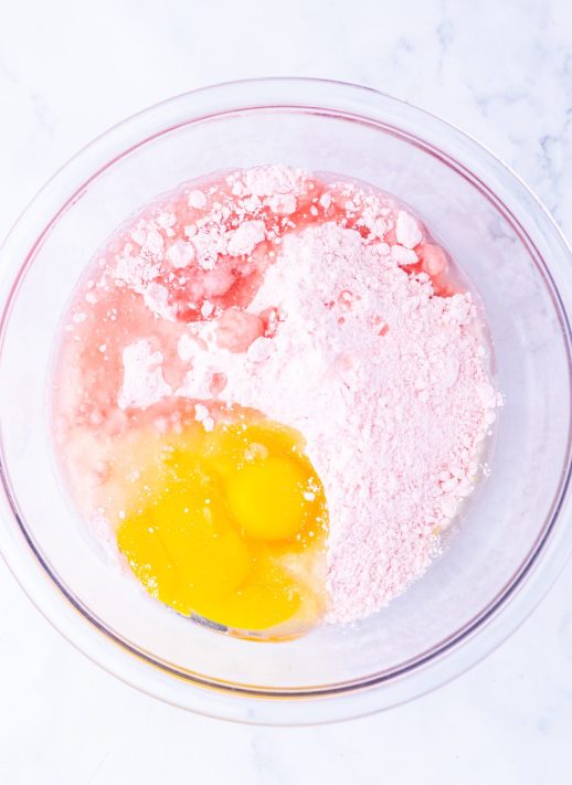 A bowl strawberry cake mix, eggs and oil.