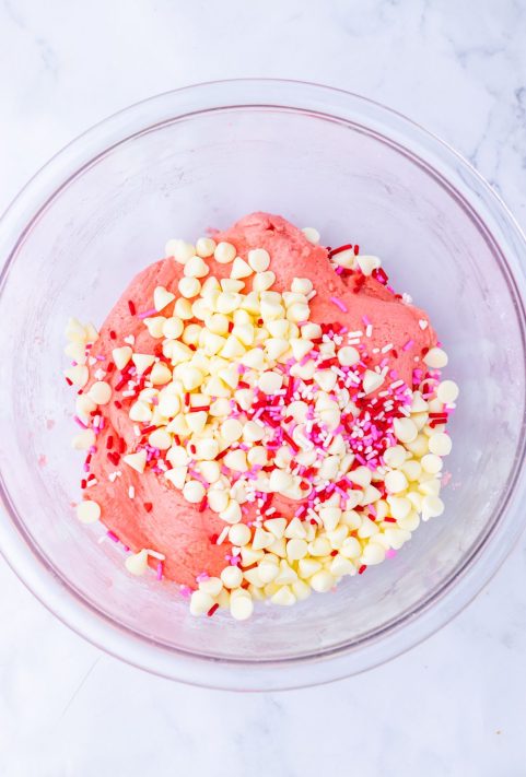 White chocolate chips and sprinkles being added to Strawberry Crunch Cookie batter.