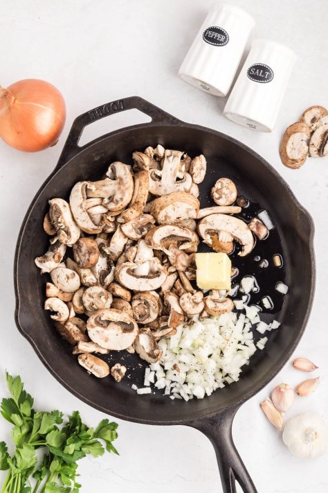 A skillet with oil, salt, pepper, mushrooms, onion, and butter.
