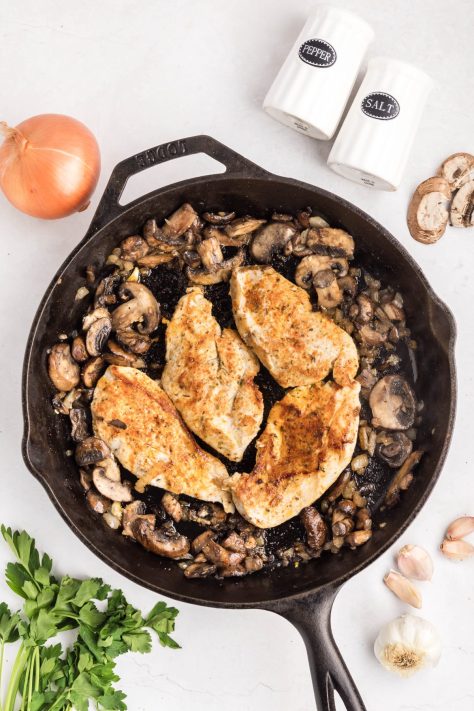 Chicken cooking in a skillet with a mushroom mixture.