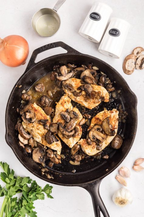 Mushroom and onion mixture being spooned over some chicken in a skillet.
