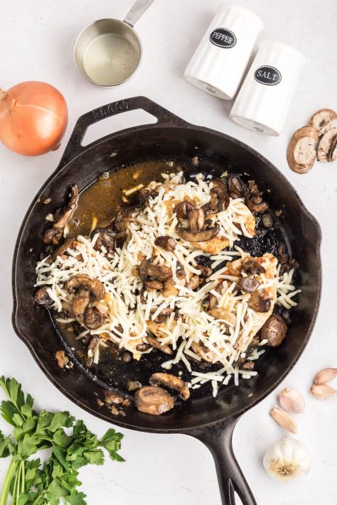 Cheese being added on top of mushrooms in a skillet.