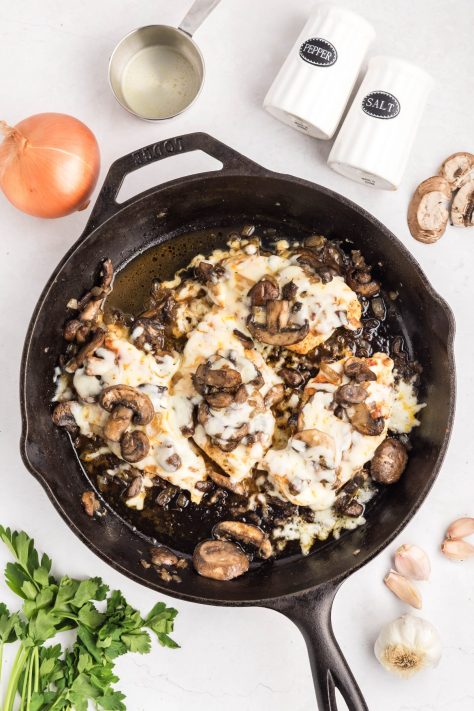 Cheese and mushroom mixture smothering chicken in a skillet.