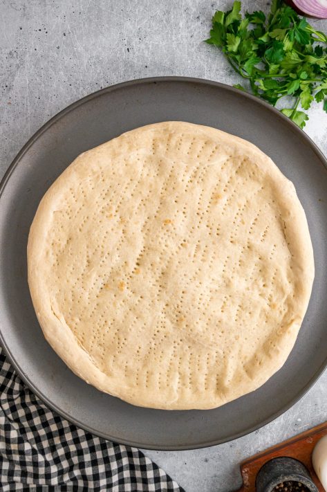 An unbaked pizza crust with holes pricked in it.