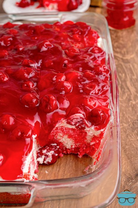 A glass baking dish with a piece of Cherry poke Cake missing.