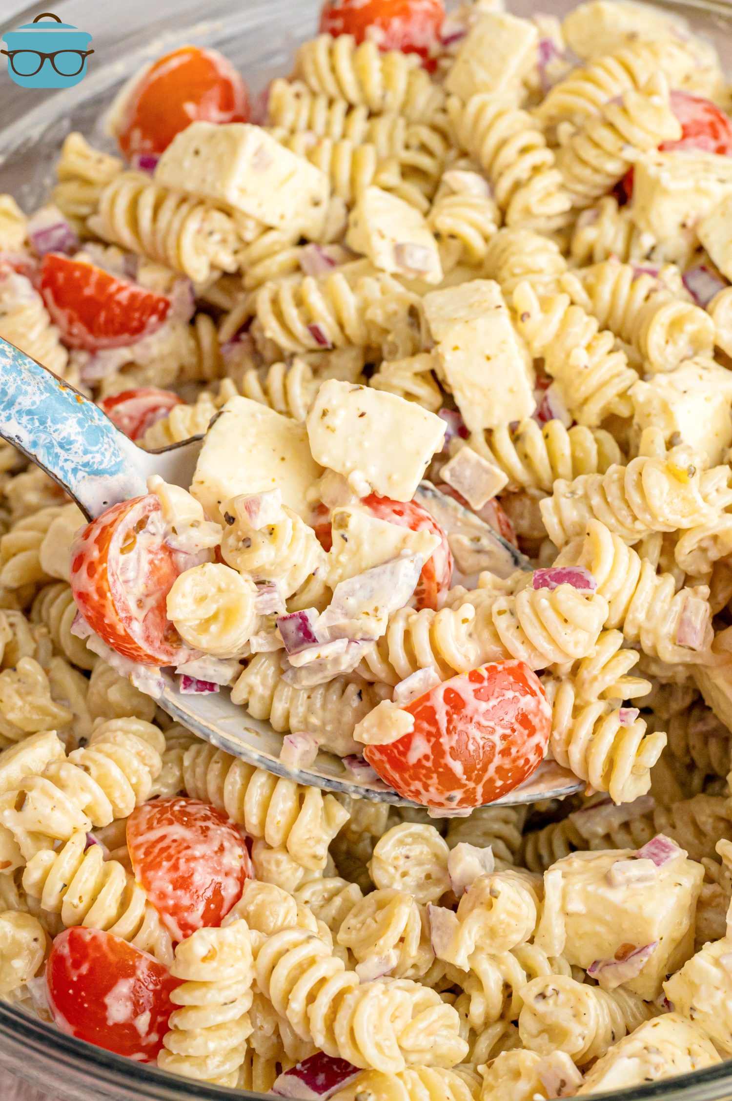 A metal spoon getting a scoop of Caesar Basil Pasta Salad from the bowl.
