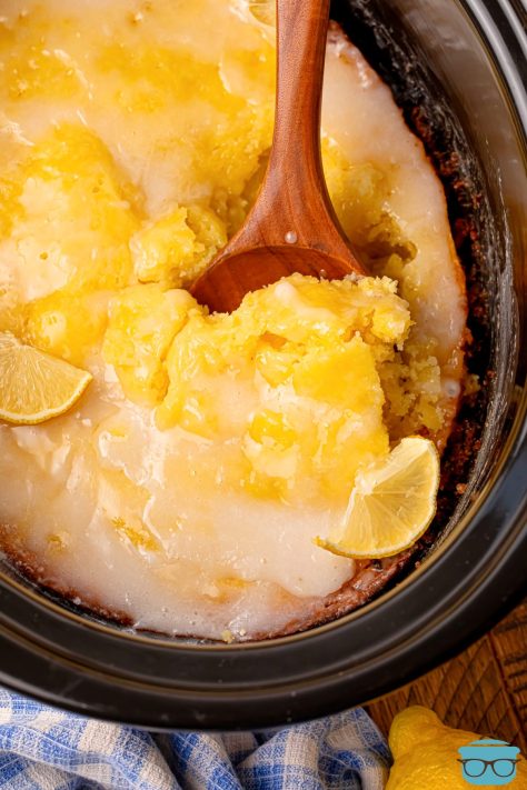 A wooden serving spoon getting a scoop of Lemon Spoon Cake from the Slow Cooker.