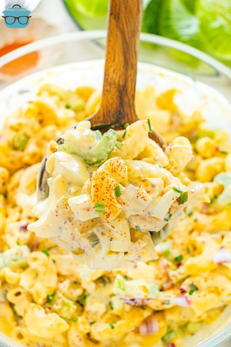 A bowl of Deviled Egg Macaroni Salad with a wooden spoon stirring it.