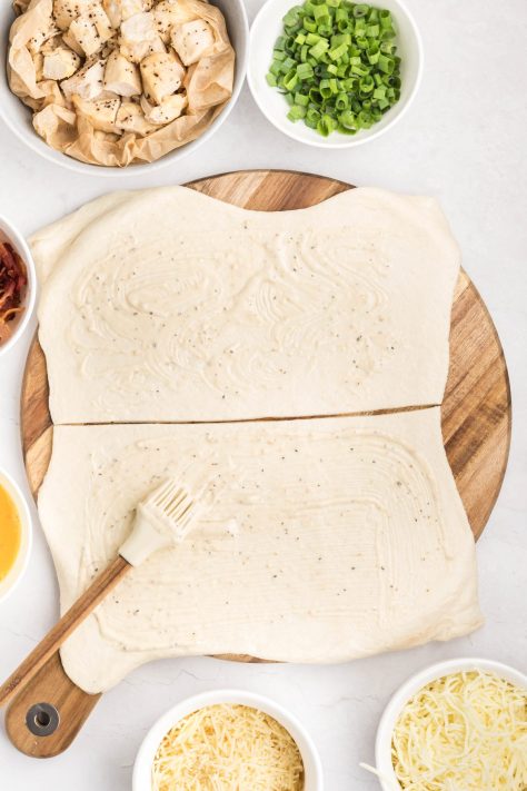 Pizza dough cut and caesar dressing spread out over it.