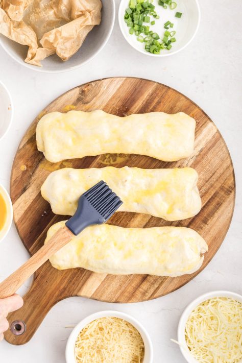 Pastry brush brushing an egg on unbaked chicken bakes.