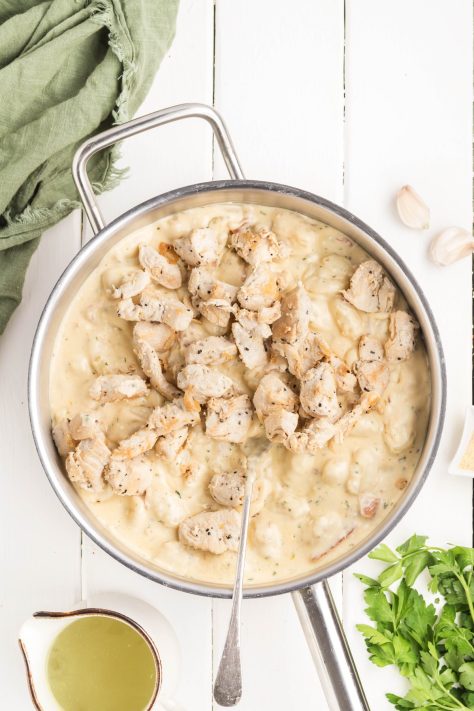 Chicken being added to gnocchi and sauce in a skillet.
