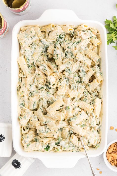 Cooked pasta being added to a creamy casserole in a dish.