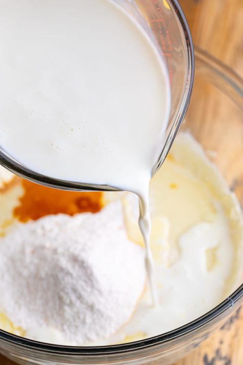 Milk being added to cream cheese, pudding mix, and vanilla extract in a bowl.