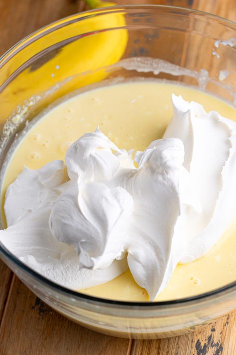 Whipped topping being added to a creamy mixture in a bowl.