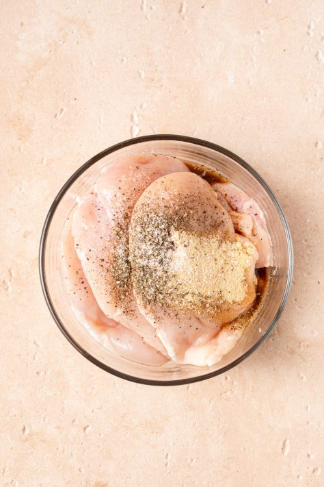 Chicken breasts and seasonings in a bowl.