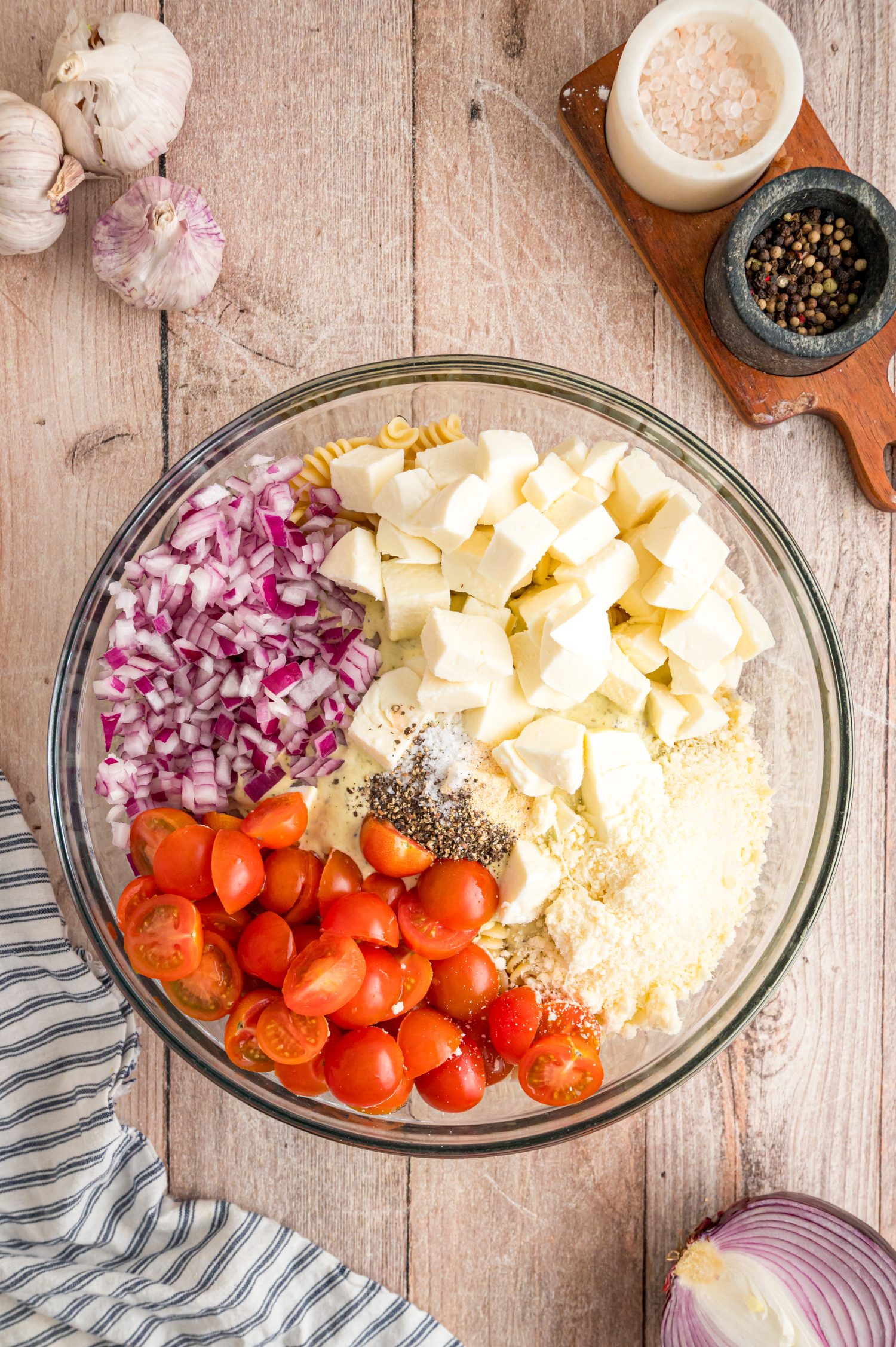 All the ingredients for Caesar Basil Pasta Salad in a bowl waiting to be mixed.