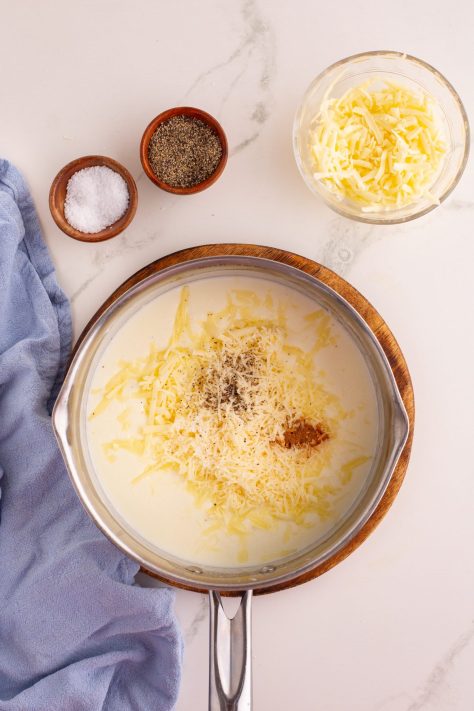 Cheeses and seasonings being added to a sauce mixture in a skillet.