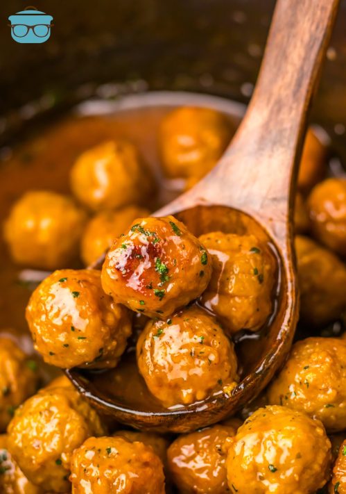 A wooden spoon getting a few Root Beer Meatballs from the Crock Pot.