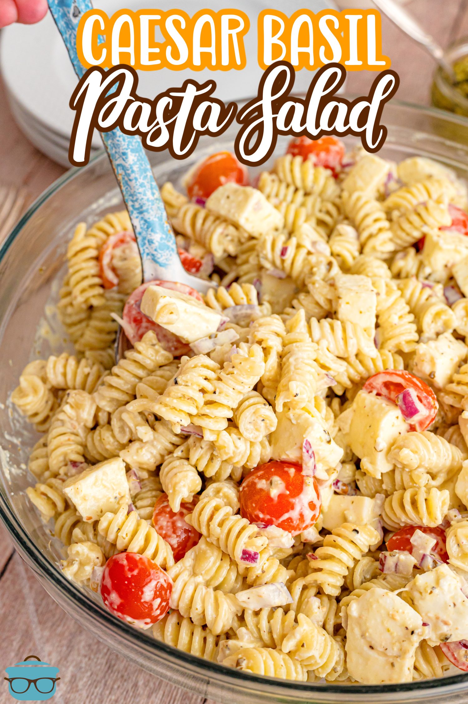 A glass bowl of Caesar Basil Pasta Salad with a serving spoon.