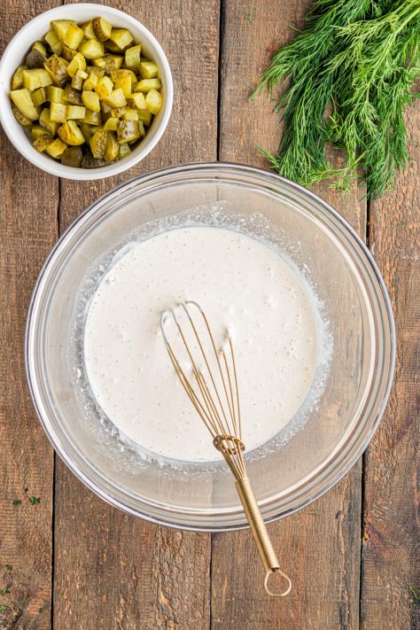 A whisk in a bowl of sauce for the potato salad.