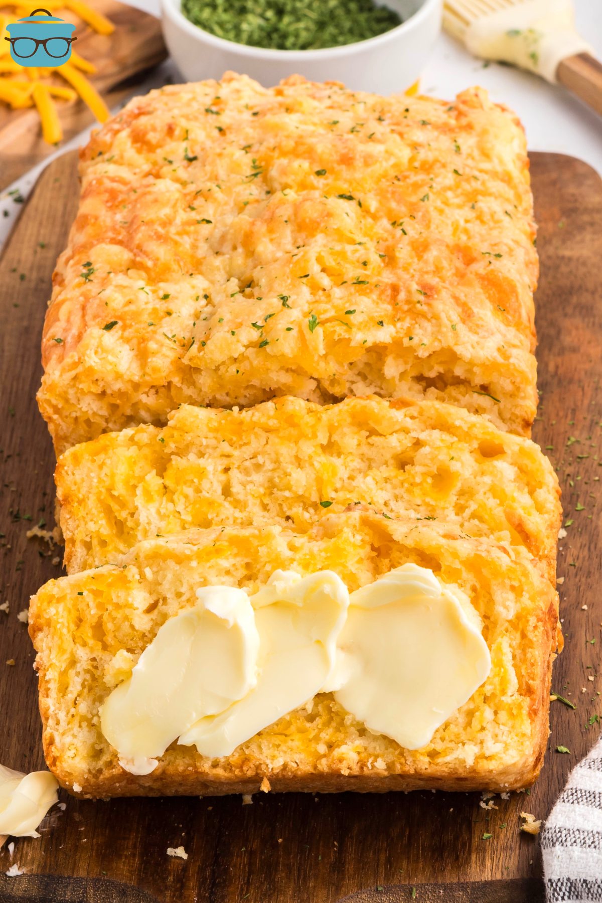 A few slices of Cheddar Bay Biscuit Bread in front of the rest of the loaf, with some butter smeared. 