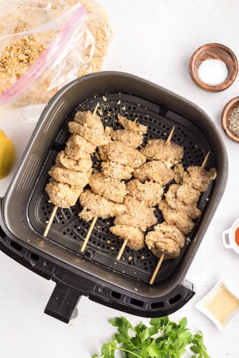Unbaked and coated chicken skewers in an Air Fryer basket.