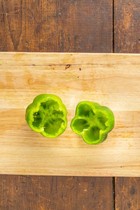 Peppers with their tops cut off on a cutting board.