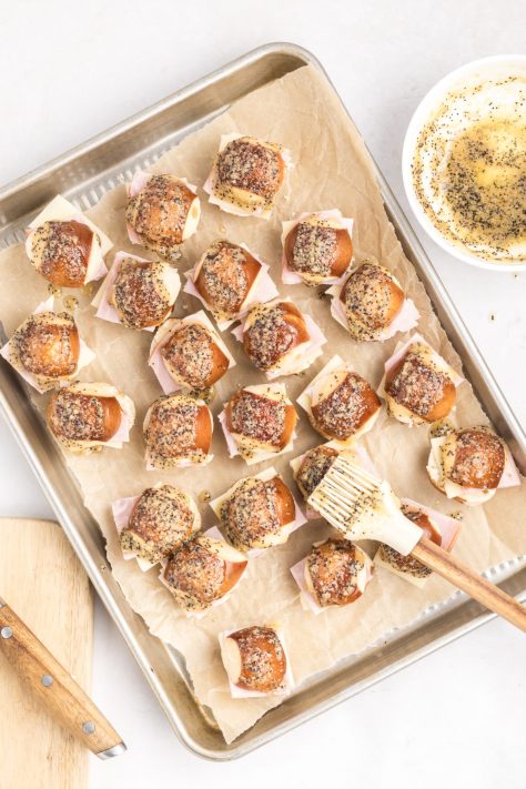 A pastry brush brushing the tops of pretzel buns.