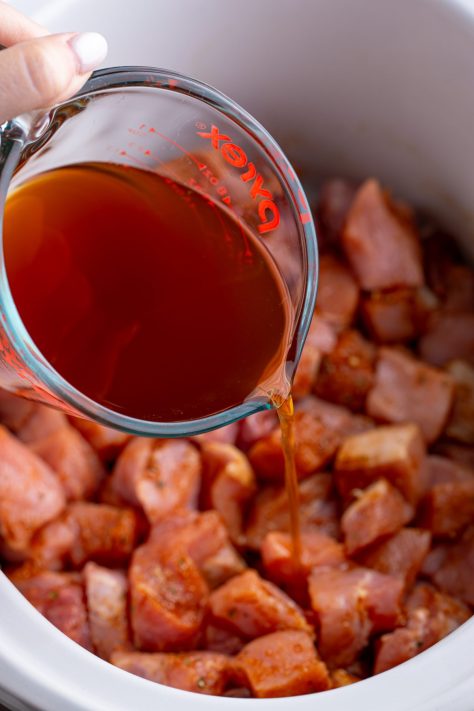Beef stock being poured over pork bites.