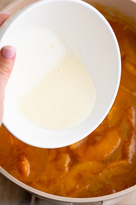 Peach juice and cornstarch slurry being added to a peach mixture.