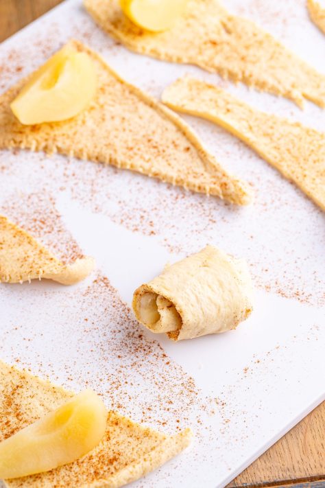 Crescent roll dough with pear pieces being rolled up.