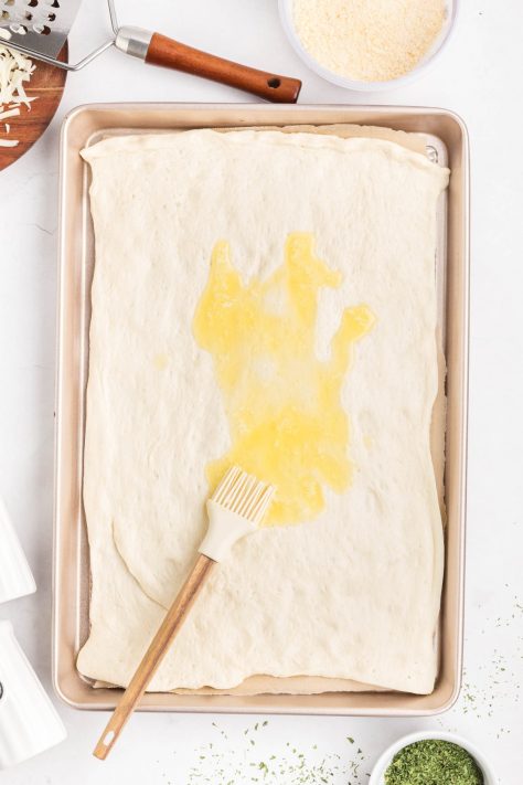 Melted butter being brushed on pizza dough.