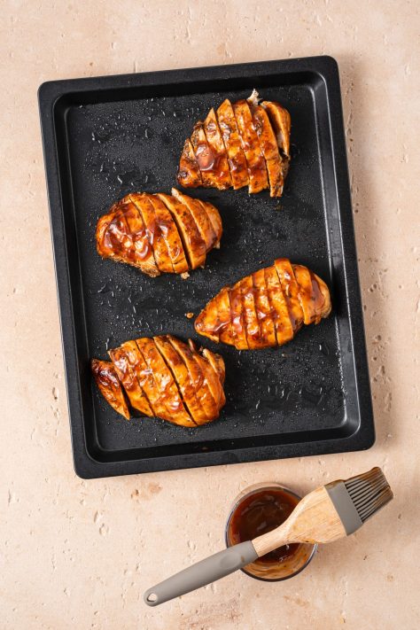 BBQ sauce coated sliced chicken breast on a baking sheet.