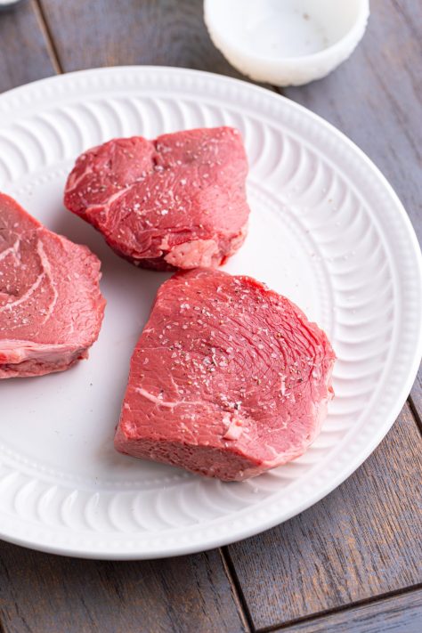 Steaks being seasoned on a plate.