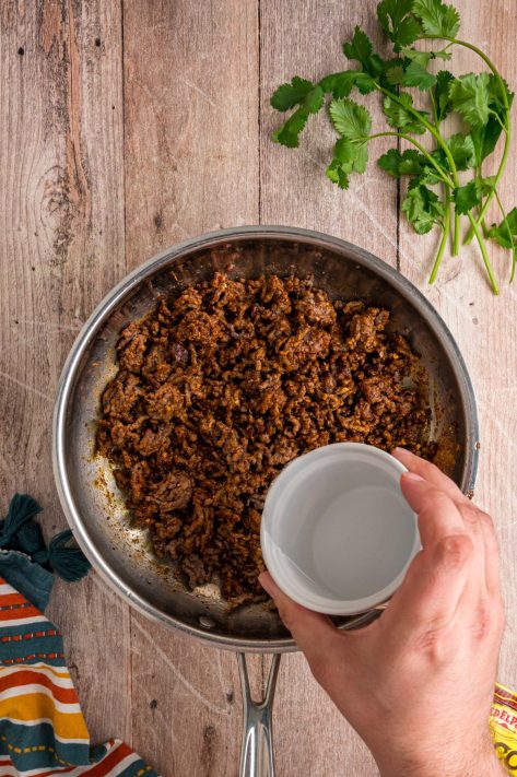 Water being added to taco seasoning in a skillet.