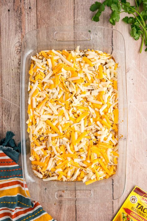 Shredded cheese over meat and rice in a baking dish.