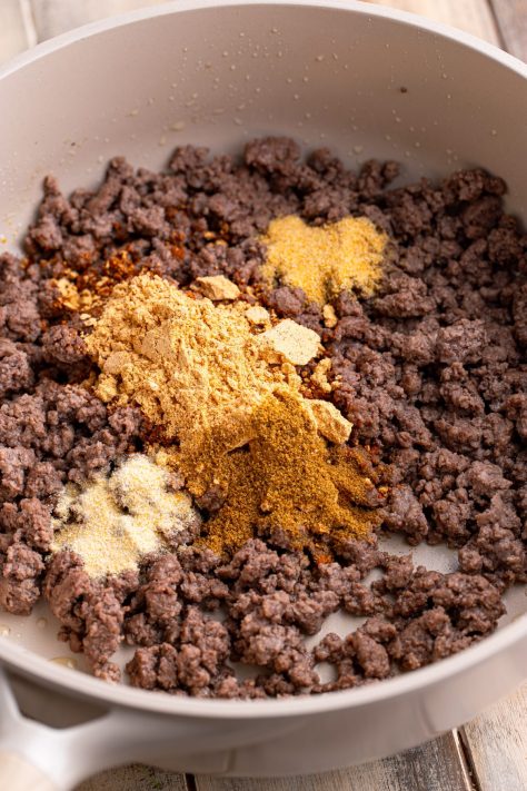 Spices being added to a skillet of cooked ground beef.