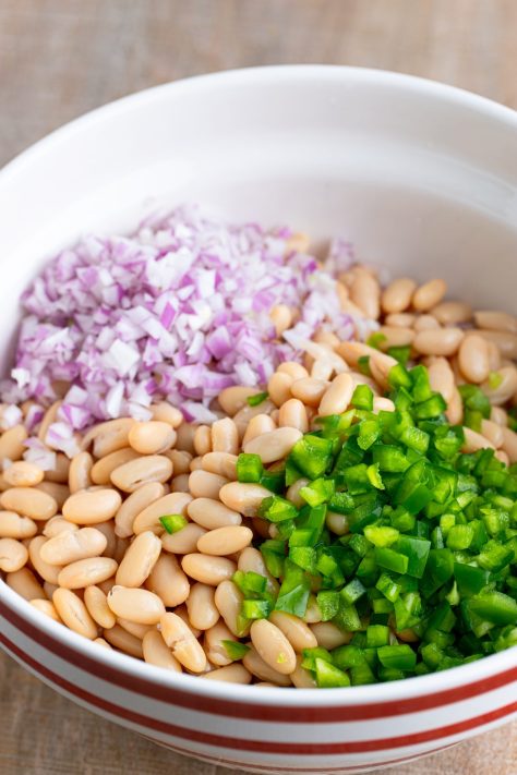Green peppers, onions, and beans added to a dill sauce in a bowl.