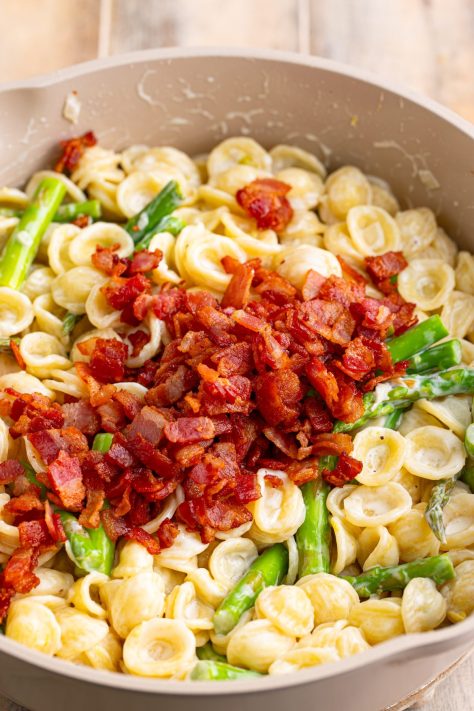 Bacon being stirred in a pasta and asparagus dish.