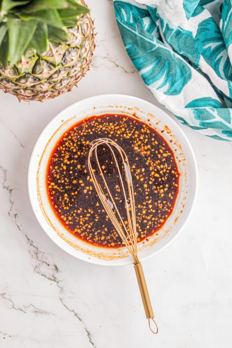 A bowl of olive oil, soy sauce, honey, garlic, and ground ginger being whisked together.
