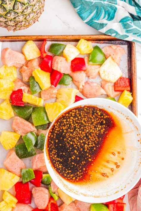 A bowl of sauce being poured over a sheet pan with a bunch of pieces.
