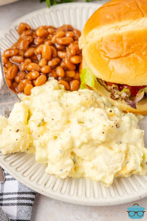A plate with a sandwich, some baked beans, and a pile of Amish Potato Salad.