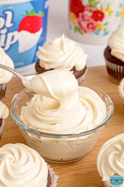 A spoon getting a scoop of Cool Whip Frosting from a small bowl.