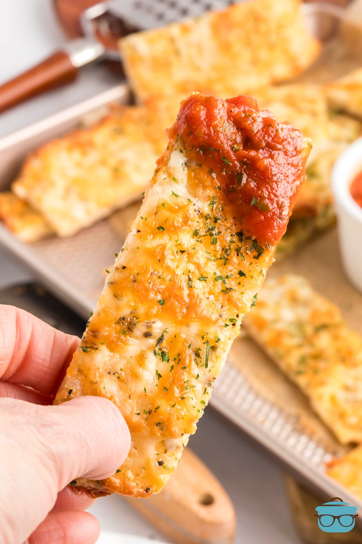 A hand holding a piece of Garlic Cheese Bread with pizza sauce on the end.
