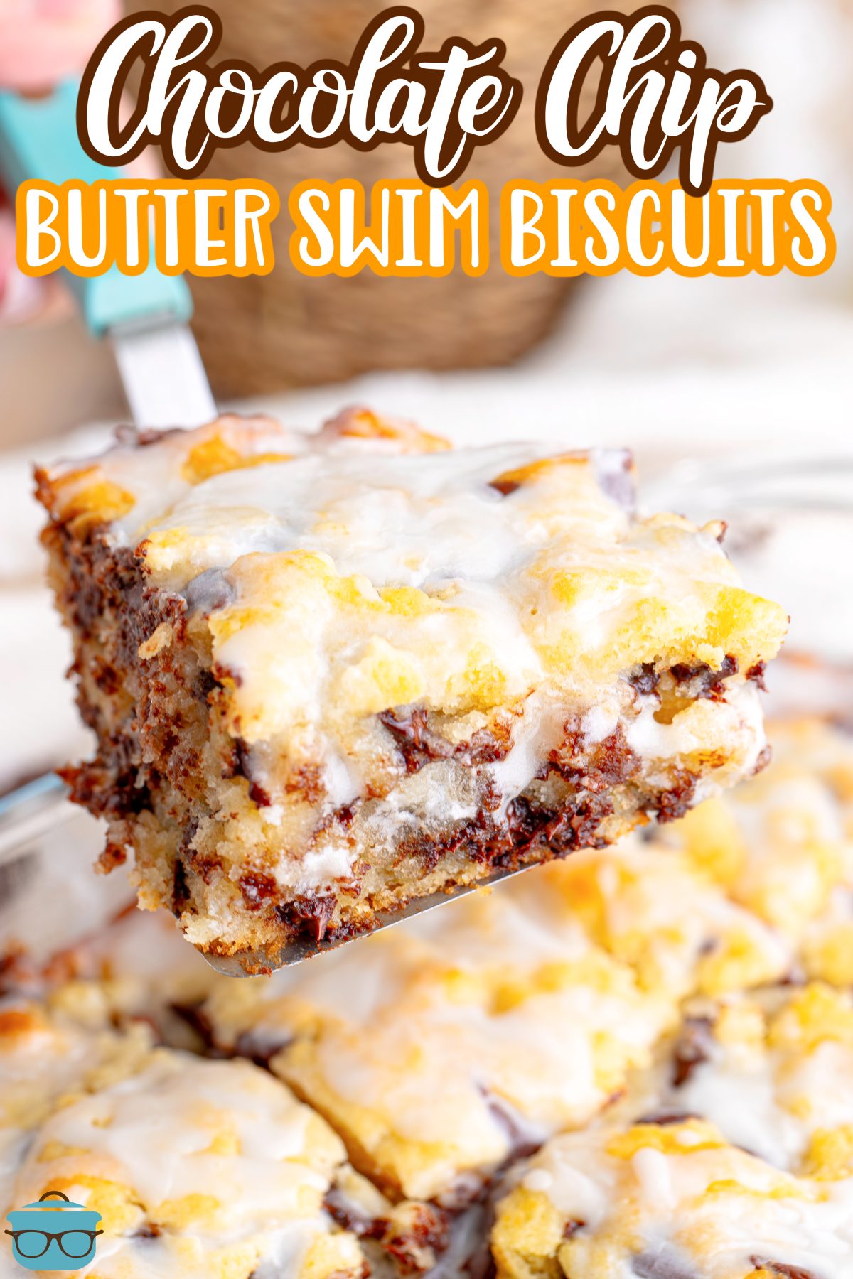 A serving utensil holding up a Chocolate Chip Butter Swim Biscuit above the baking dish that's full of them.