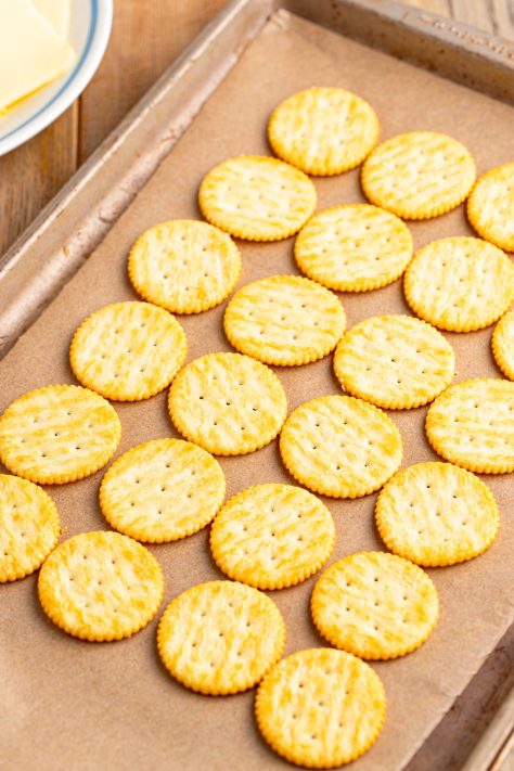 Ritz crackers laid out on a lined baking sheet.