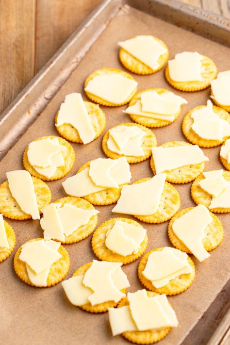 Slices of cheese on top of crackers on a lined baking sheet.