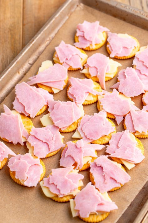 Ham and cheese over crackers on a lined baking sheet.