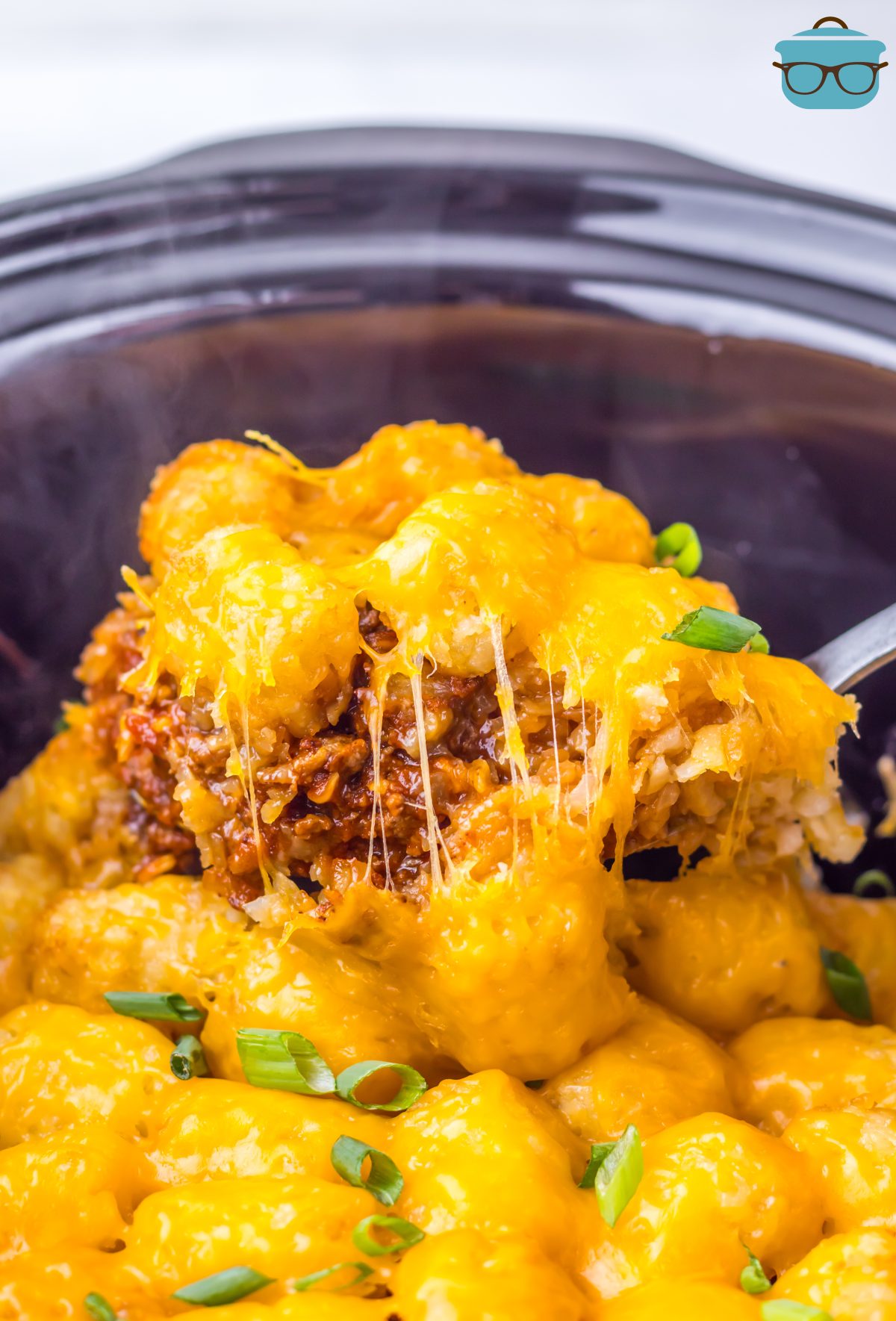 Looking down into a Slow Cooker where a utensil is getting some Chili Cheese Tater Tot Casserole.