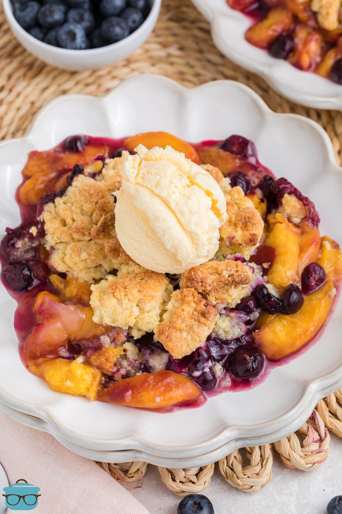 A fluted dessert plate with a scoop of Peach Blueberry Cobbler and a scoop of ice cream.